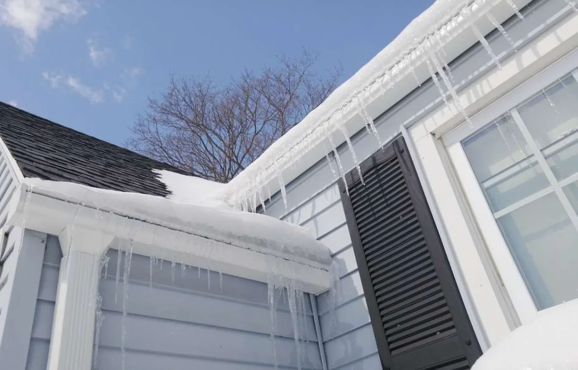 Ice dam on a gutter above gray siding